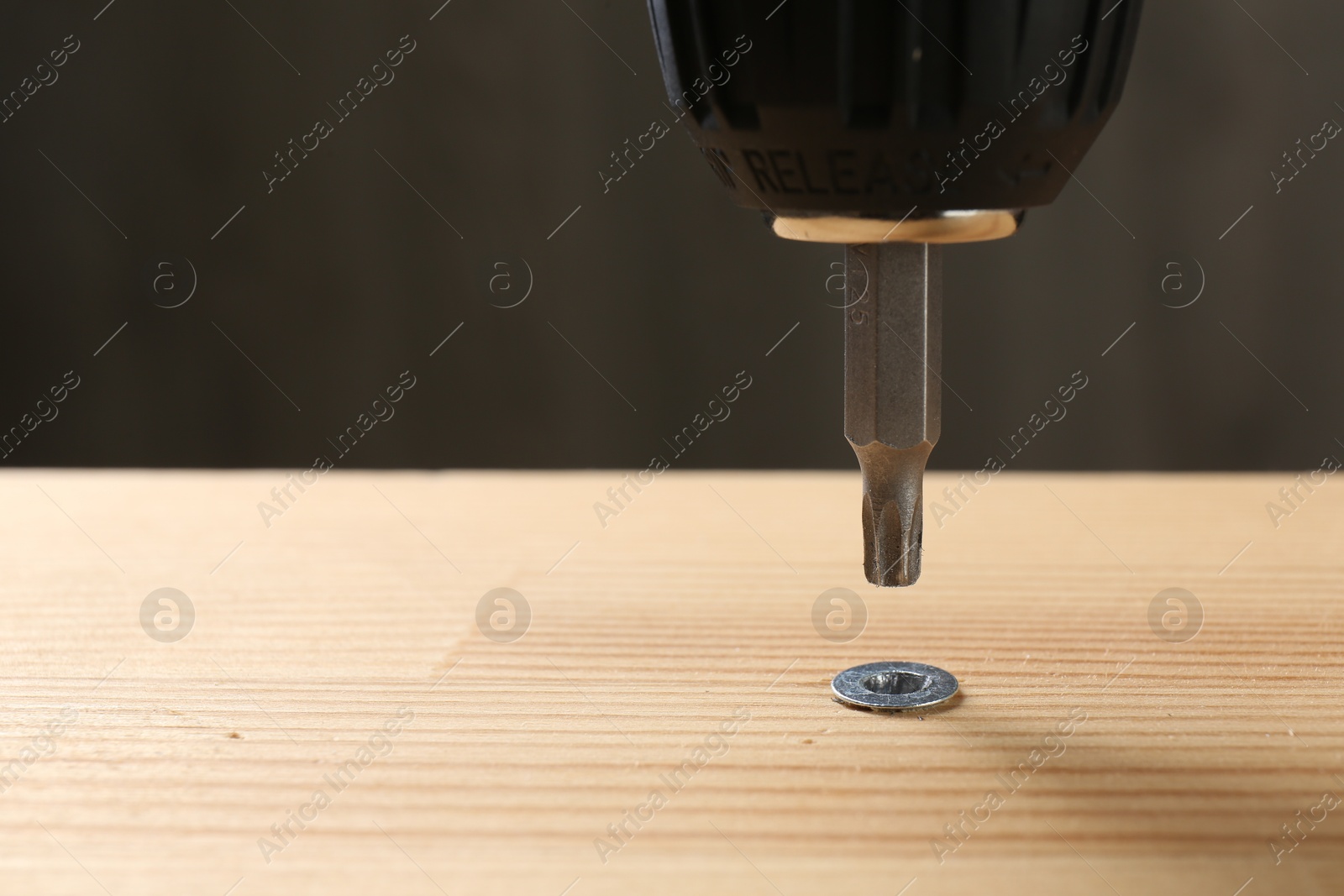 Photo of Screwing screw into wooden plank against gray background, closeup. Space for text