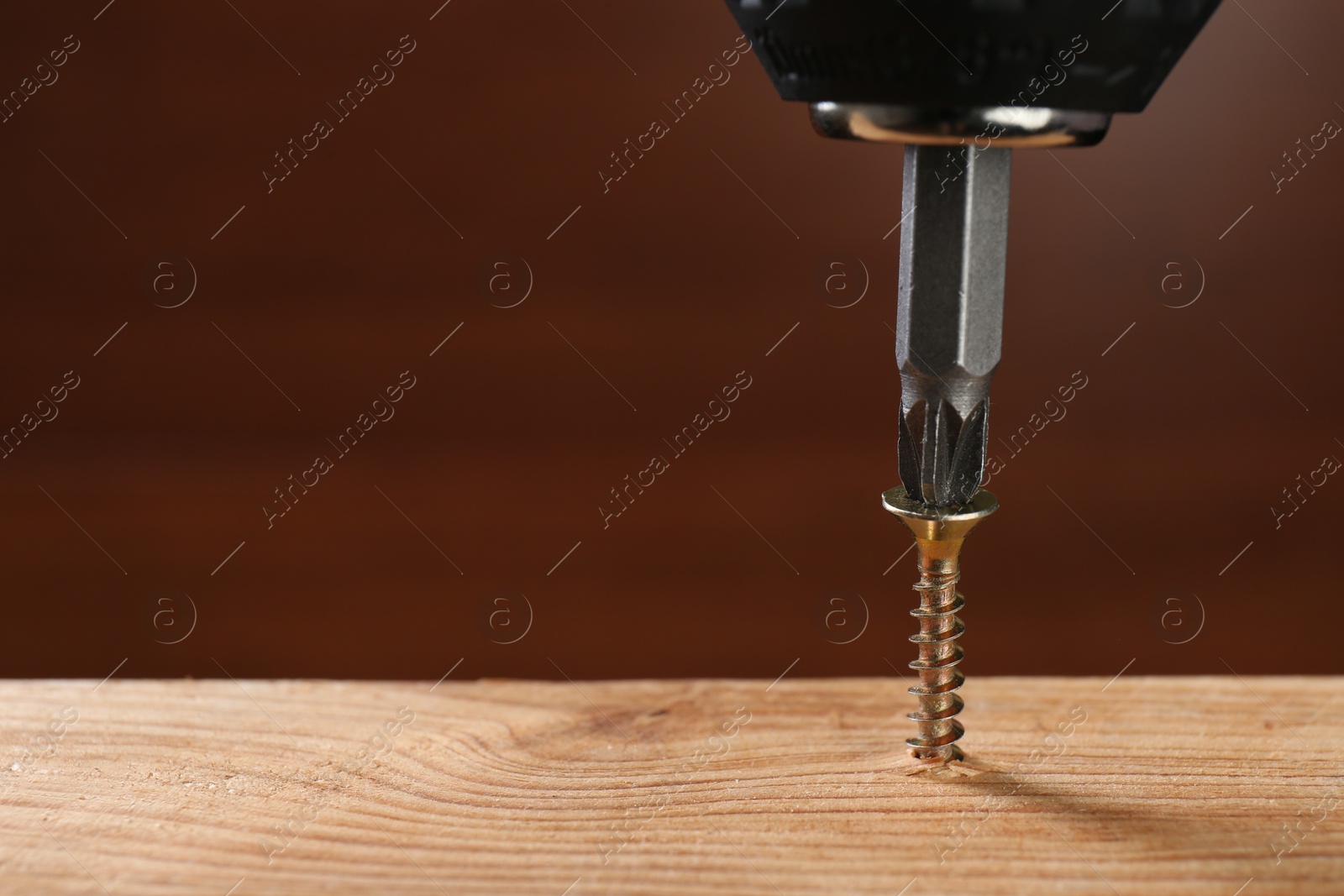 Photo of Screwing screw into wooden plank against brown background, closeup. Space for text