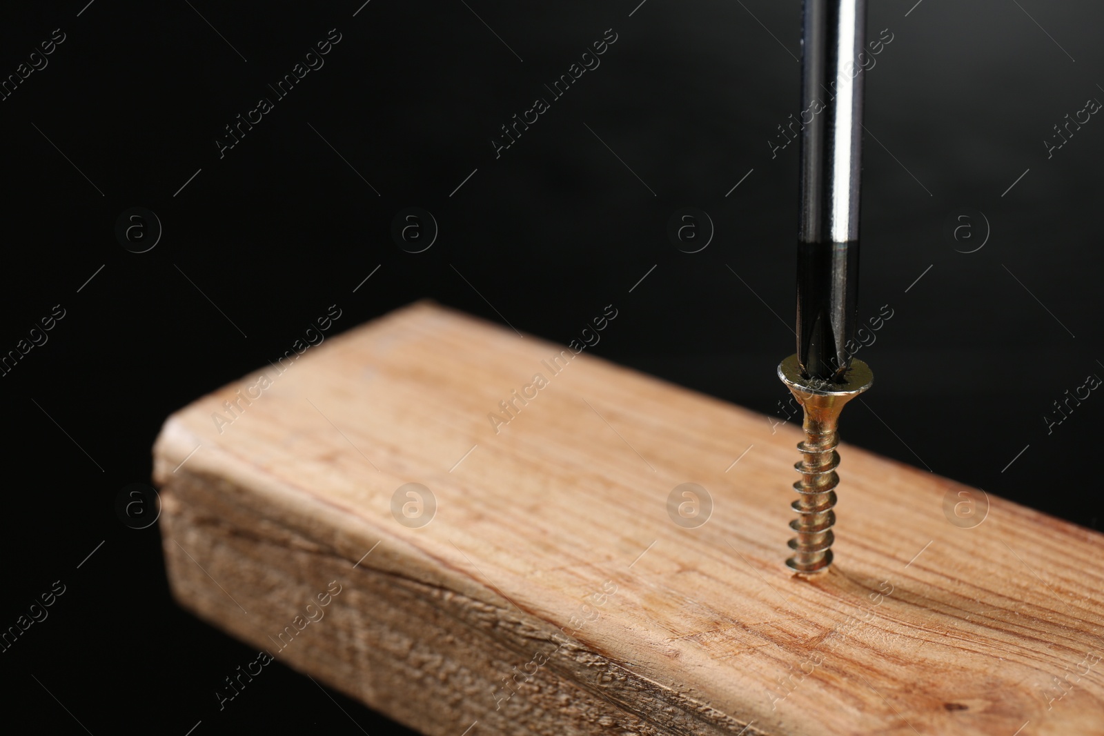 Photo of Screwing screw into wooden plank against dark background, closeup