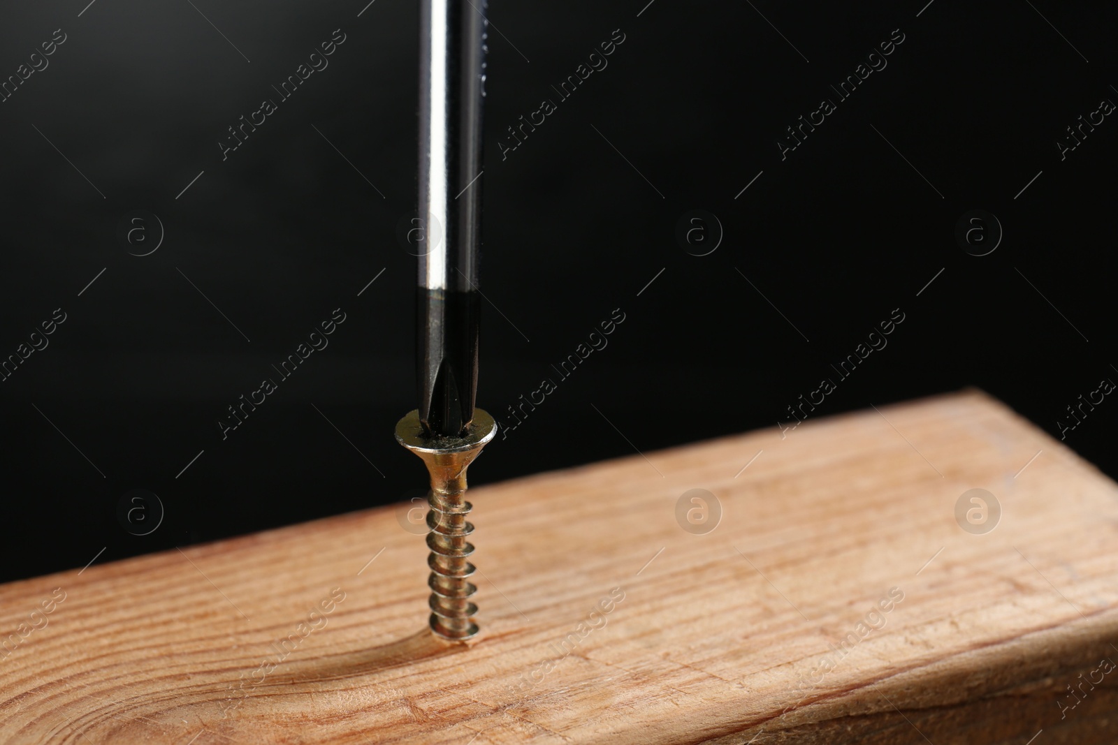 Photo of Screwing screw into wooden plank against dark background, closeup