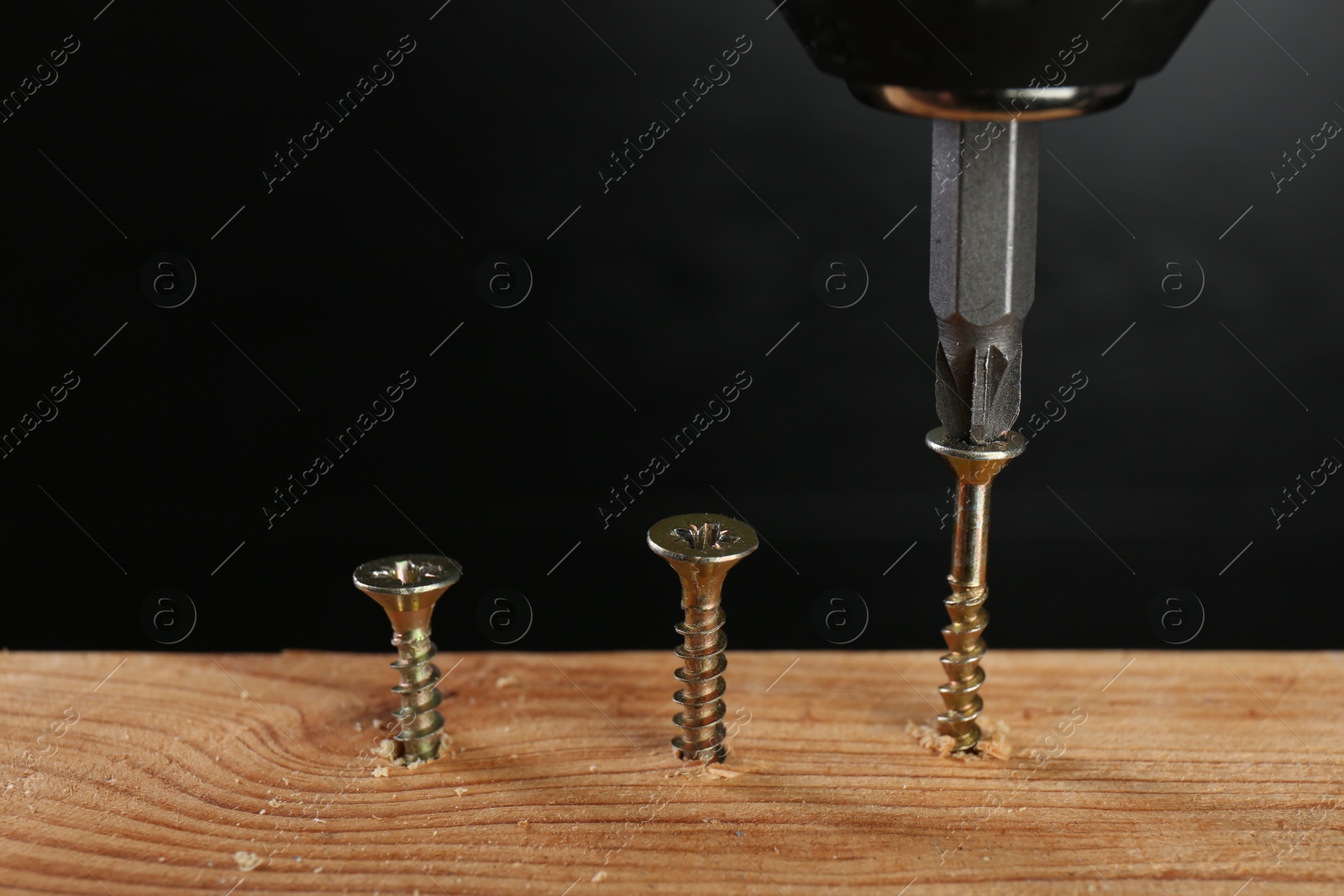 Photo of Screwing screw into wooden plank against dark background, closeup