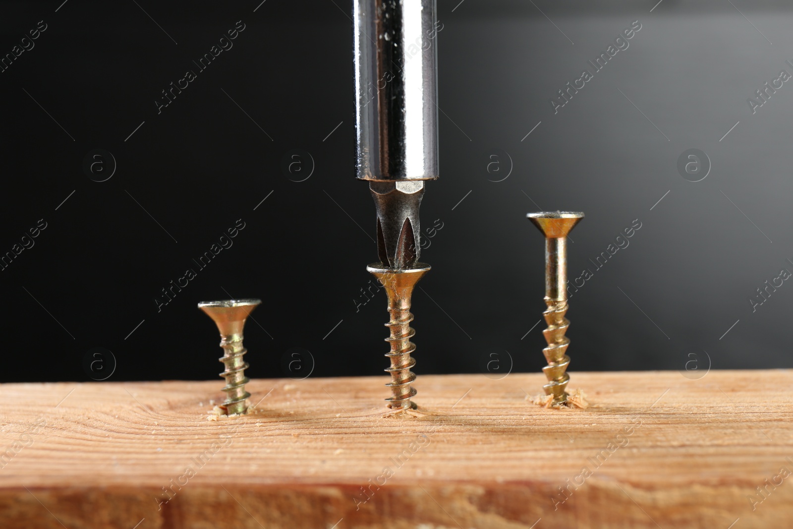 Photo of Screwing screw into wooden plank against dark background, closeup