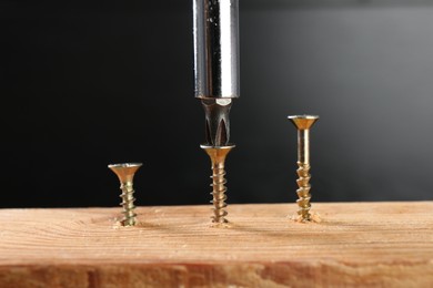 Photo of Screwing screw into wooden plank against dark background, closeup