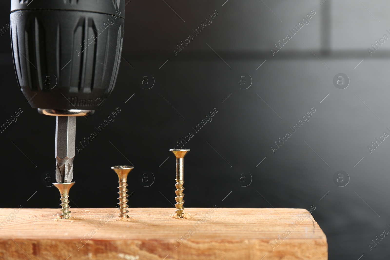 Photo of Screwing screw into wooden plank against dark background, closeup. Space for text