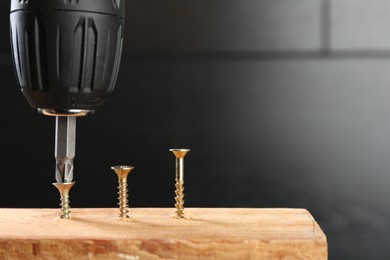 Photo of Screwing screw into wooden plank against dark background, closeup. Space for text