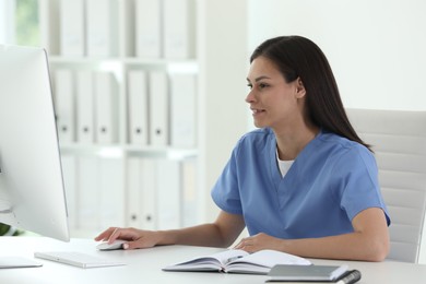 Photo of Smiling nurse working with computer at table in hospital office