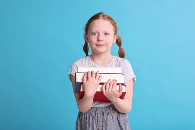 Photo of Cute girl with stack of books on light blue background