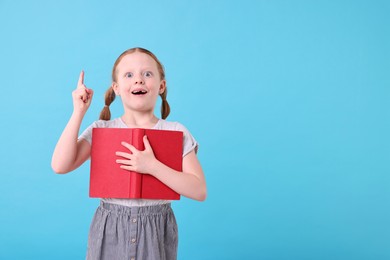 Photo of Happy girl with book on light blue background. Space for text