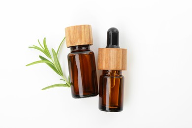 Aromatic essential oils in bottles and rosemary on white background, flat lay