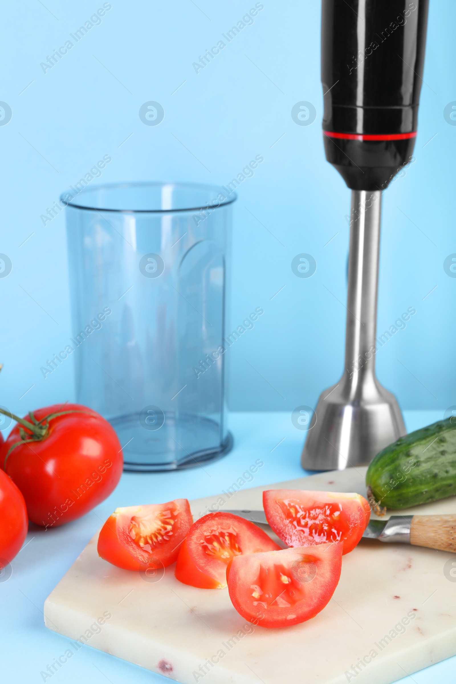 Photo of Hand blender kit, fresh vegetables and knife on light blue background