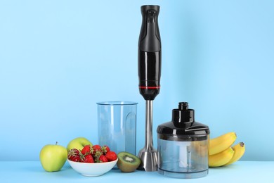 Photo of Hand blender kit, fresh fruits and strawberries on light blue background