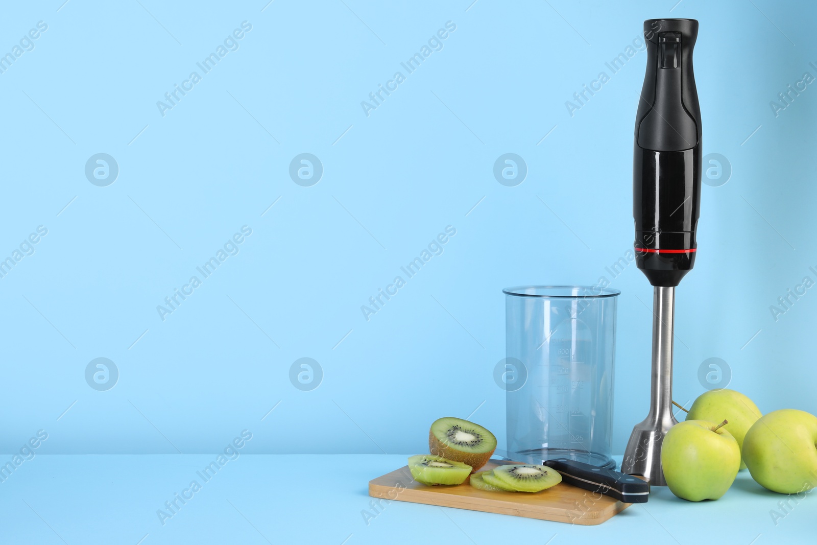 Photo of Hand blender kit, fresh fruits and knife on light blue background, space for text