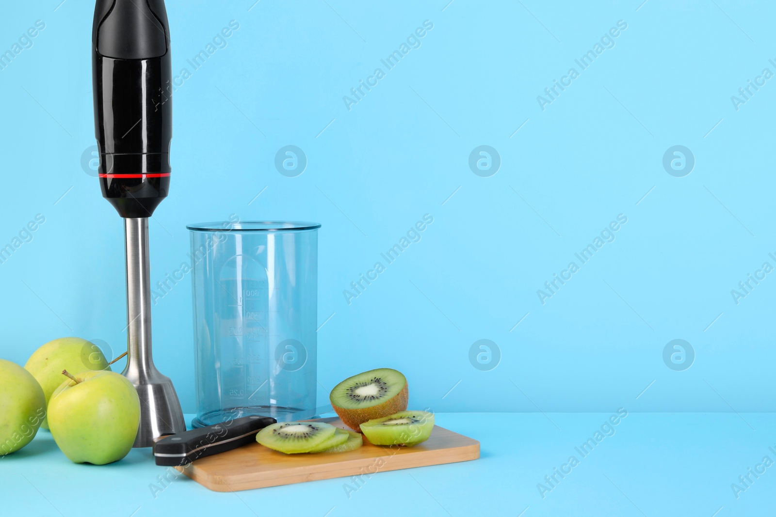 Photo of Hand blender kit, fresh fruits and knife on light blue background, space for text