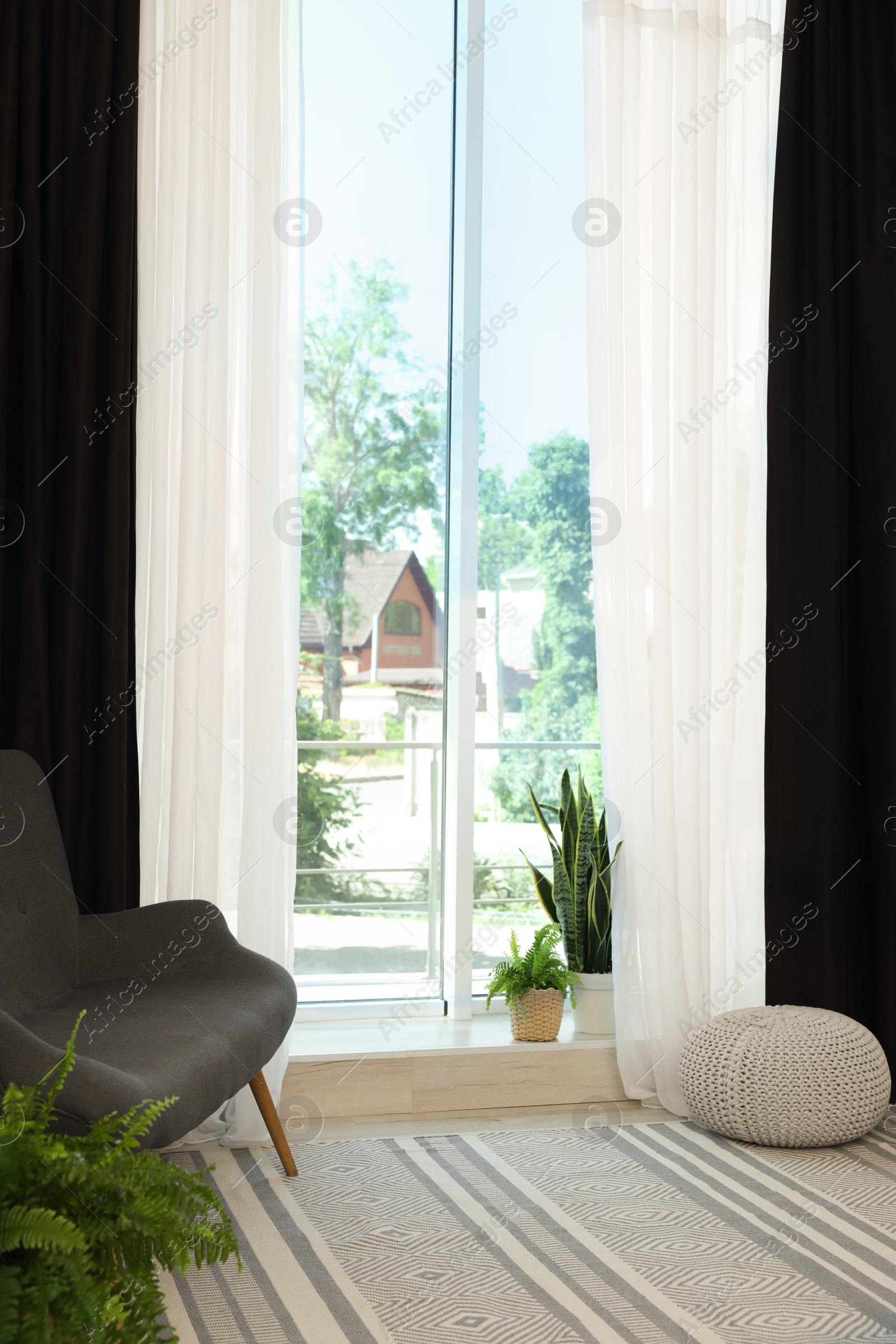 Photo of Sofa, green houseplants, pouffe and elegant curtains in room. Interior design