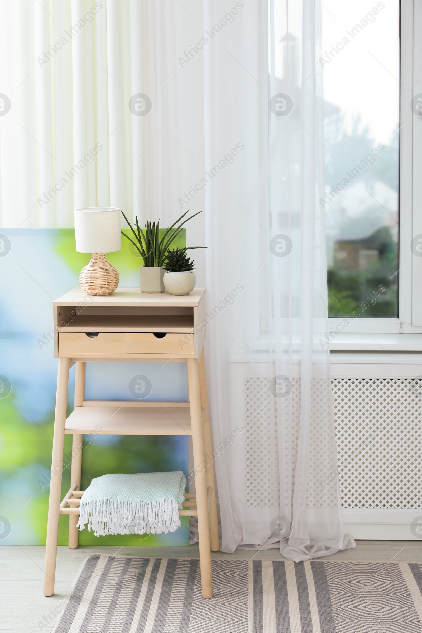 Photo of Nightstand, houseplants and lamp near window with beautiful curtain in room. Interior design