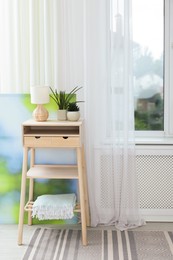 Photo of Nightstand, houseplants and lamp near window with beautiful curtain in room. Interior design