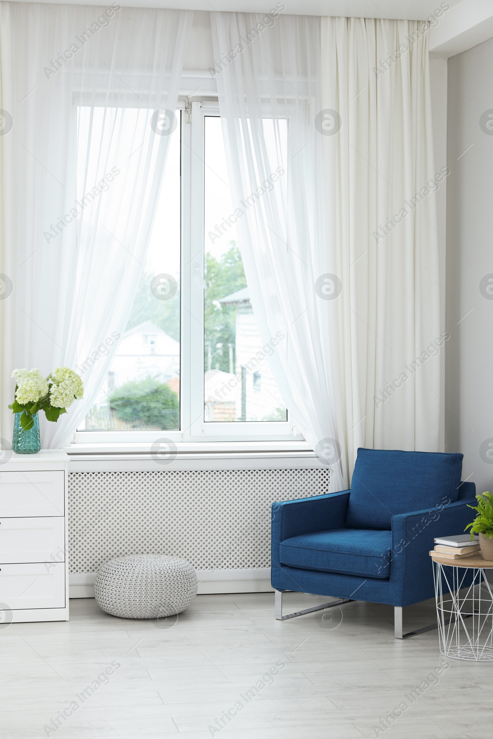 Photo of Soft armchair, side table, flowers and window with curtains in room. Interior design