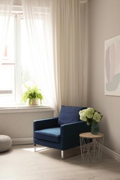 Photo of Soft armchair, side table, flowers and window with curtains in room. Interior design