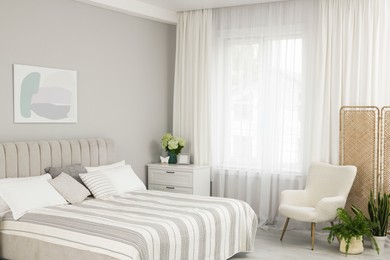 Photo of Large bed, chest of drawers, armchair and window with curtains in bedroom. Interior design