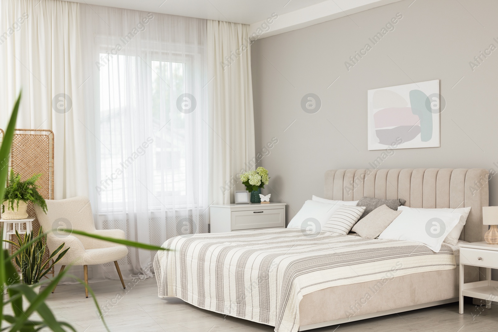 Photo of Large bed, nightstand, chest of drawers, armchair and window with curtains in bedroom. Interior design