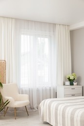 Photo of Chest of drawers, armchair and window with curtains in bedroom. Interior design