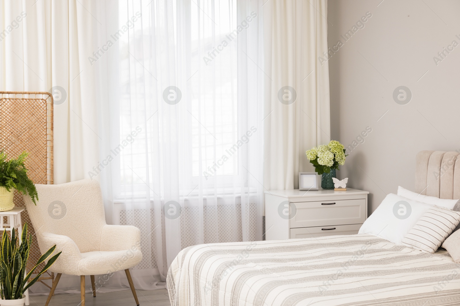 Photo of Large bed, chest of drawers, armchair and window with curtains in bedroom. Interior design