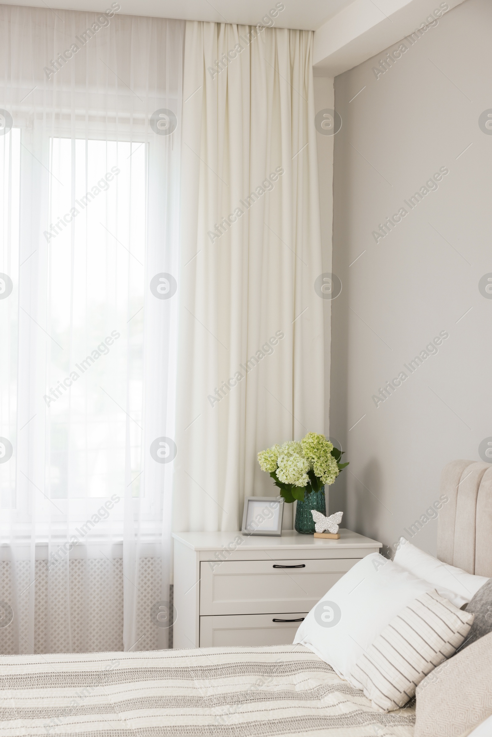 Photo of Bed, chest of drawers and window with curtains in bedroom. Interior design