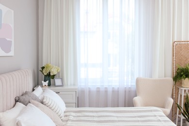 Photo of Large bed, chest of drawers, armchair and window with curtains in bedroom. Interior design