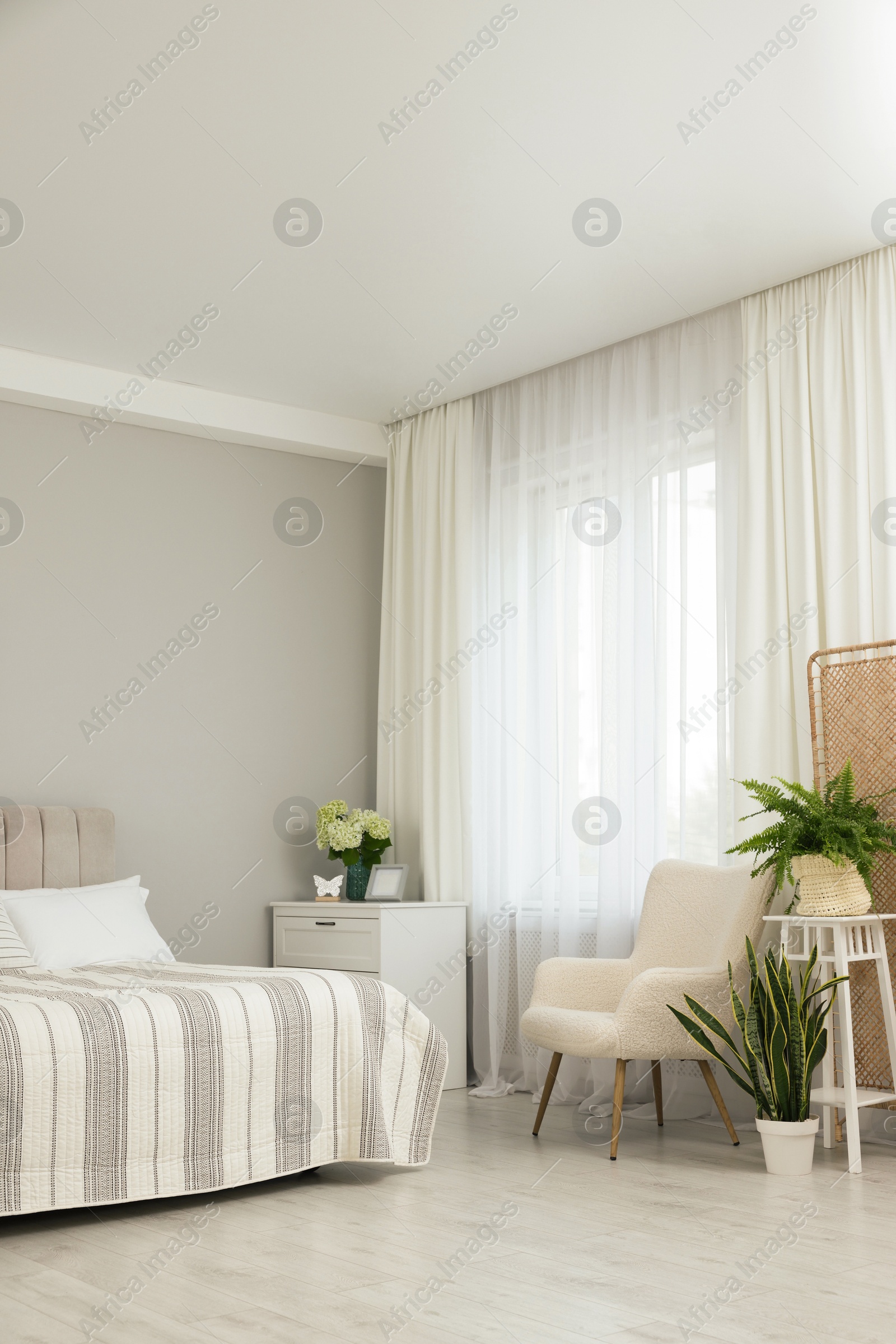 Photo of Bed, chest of drawers, armchair, houseplants and window with curtains in bedroom. Interior design