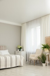 Photo of Bed, chest of drawers, armchair, houseplants and window with curtains in bedroom. Interior design