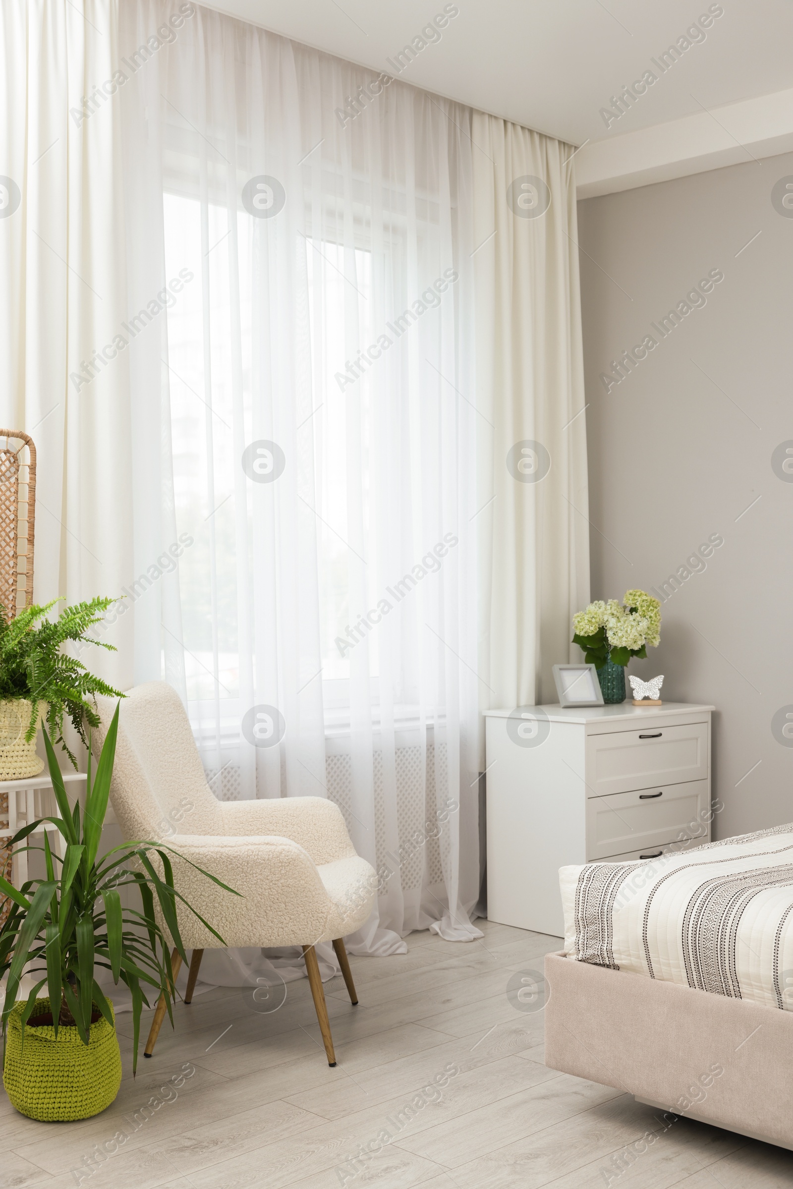 Photo of Chest of drawers, armchair, houseplants and window with curtains indoors. Interior design