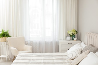 Photo of Large bed, chest of drawers, armchair and window with curtains in bedroom. Interior design