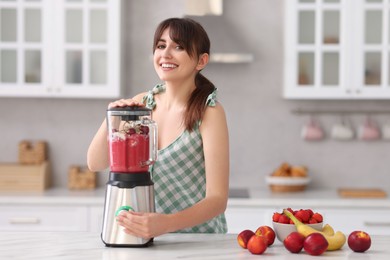 Photo of Young woman making delicious smoothie with blender at white marble table in kitchen