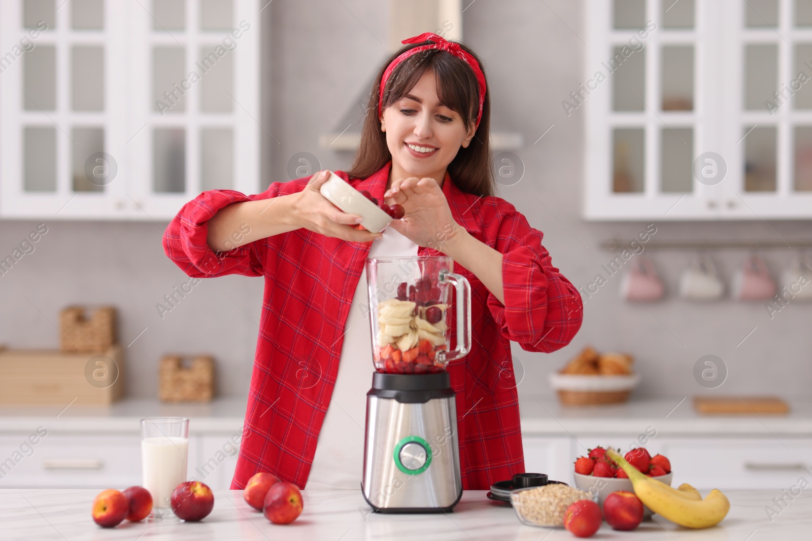 Photo of Young woman making delicious smoothie with blender at white marble table in kitchen