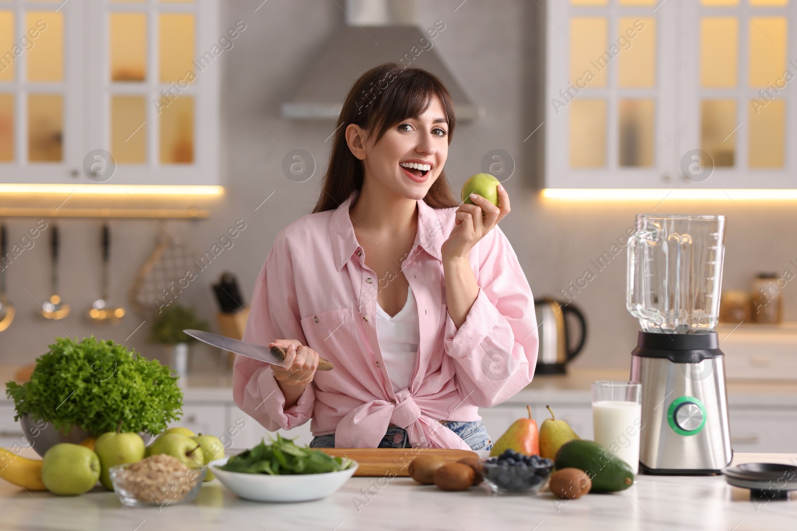 Photo of Young woman making delicious smoothie with blender at white marble table in kitchen