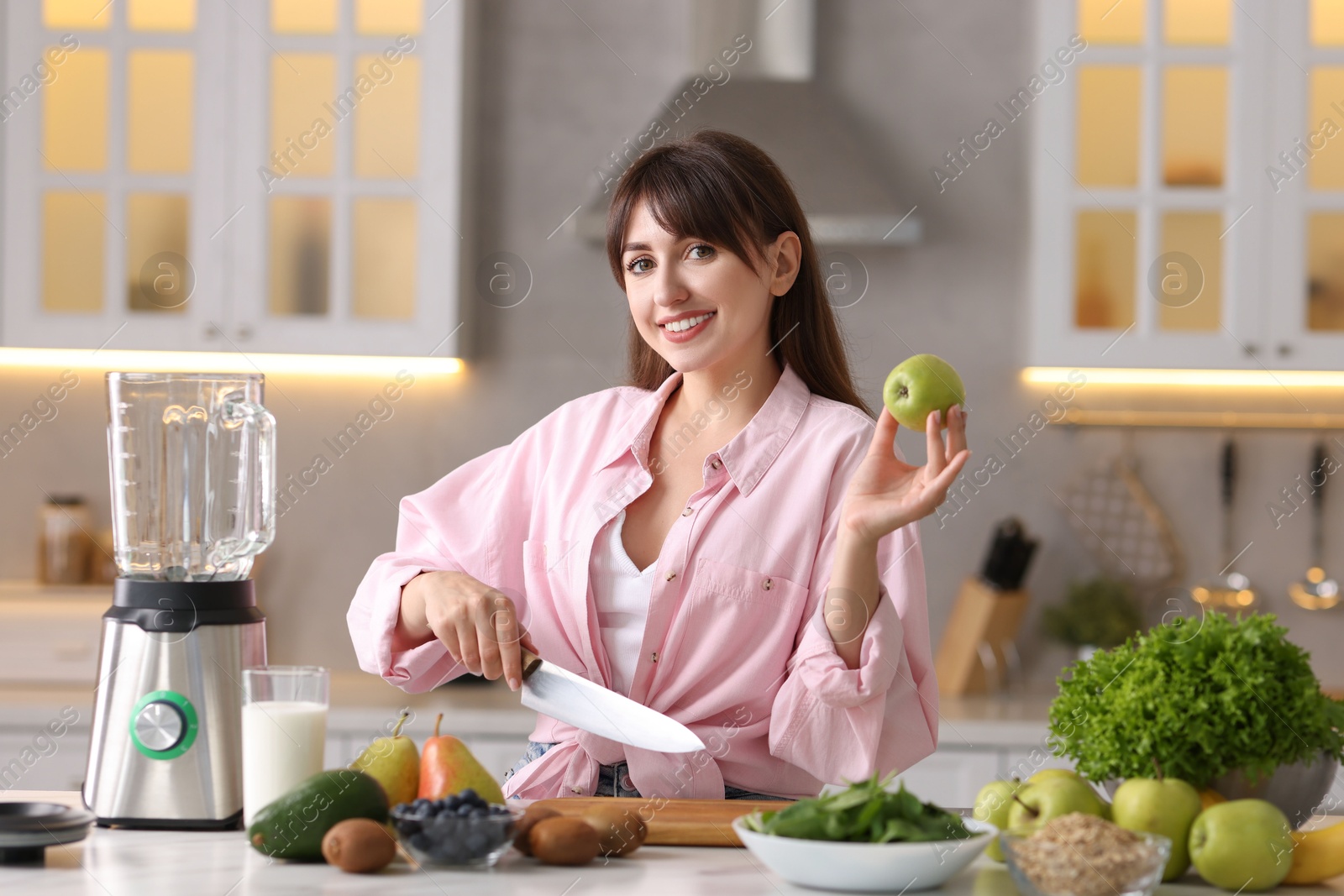 Photo of Young woman making delicious smoothie with blender at white marble table in kitchen