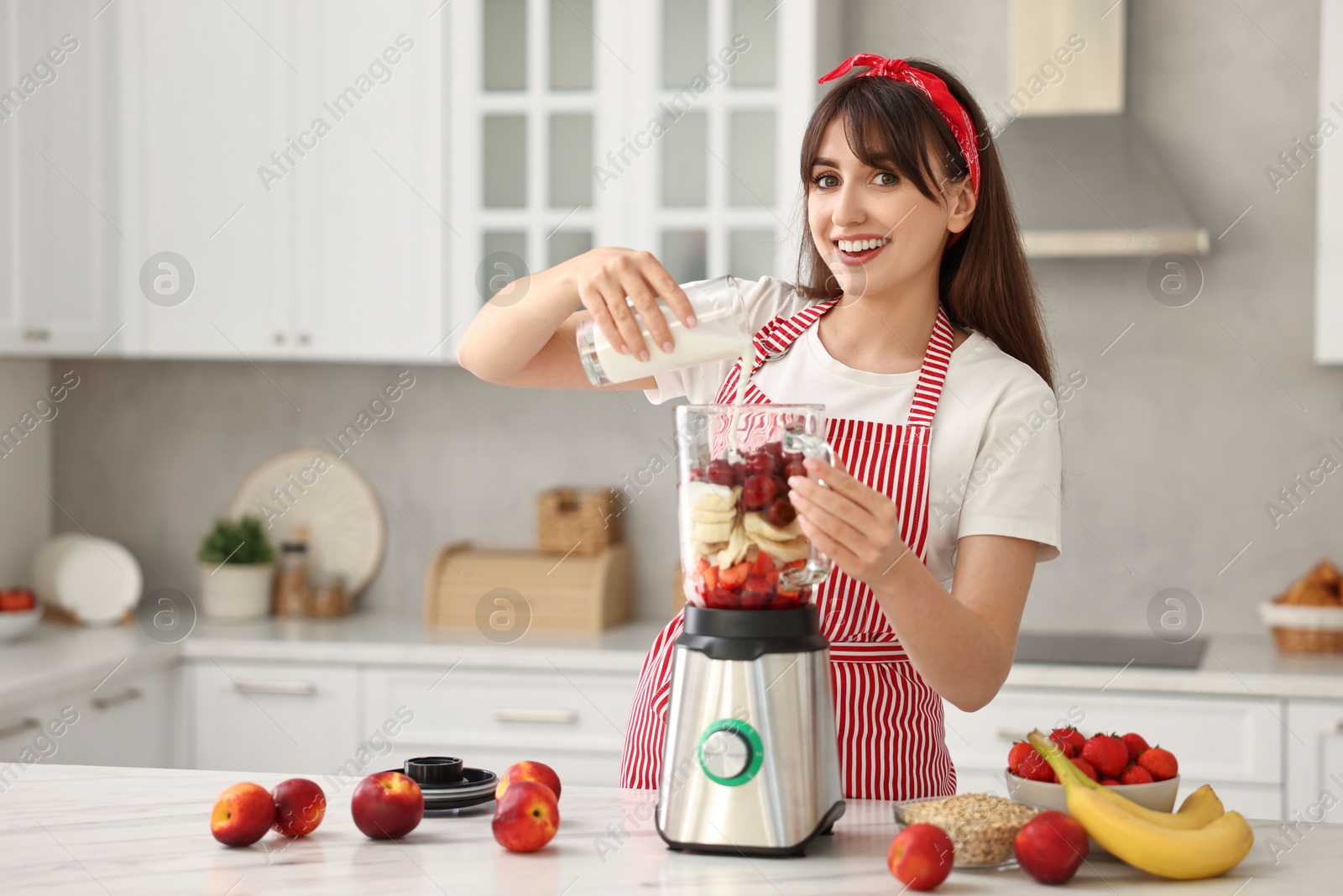 Photo of Young woman making delicious smoothie with blender at white marble table in kitchen