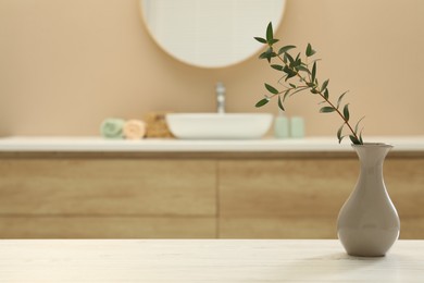 Photo of Beautiful vase with green twig on table in bathroom. Space for text