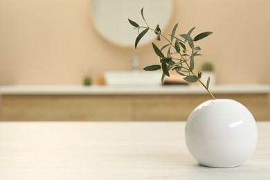 Round vase with green twig on table in bathroom. Space for text