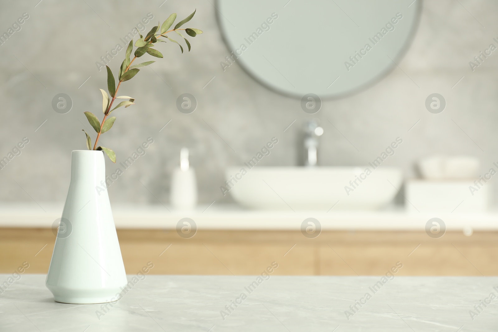 Photo of Vase with green twig on light grey marble table in bathroom, space for text