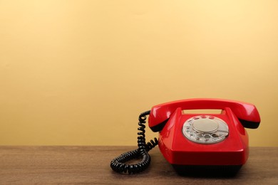 Photo of Red telephone with handset on wooden table against beige background, space for text