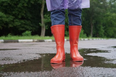 Photo of Woman wearing red rubber boots standing in puddle outdoors, closeup. Space for text