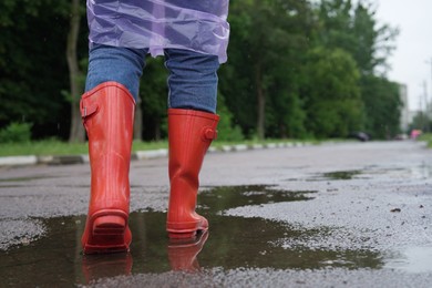 Photo of Woman in red rubber boots walking outdoors, closeup. Space for text