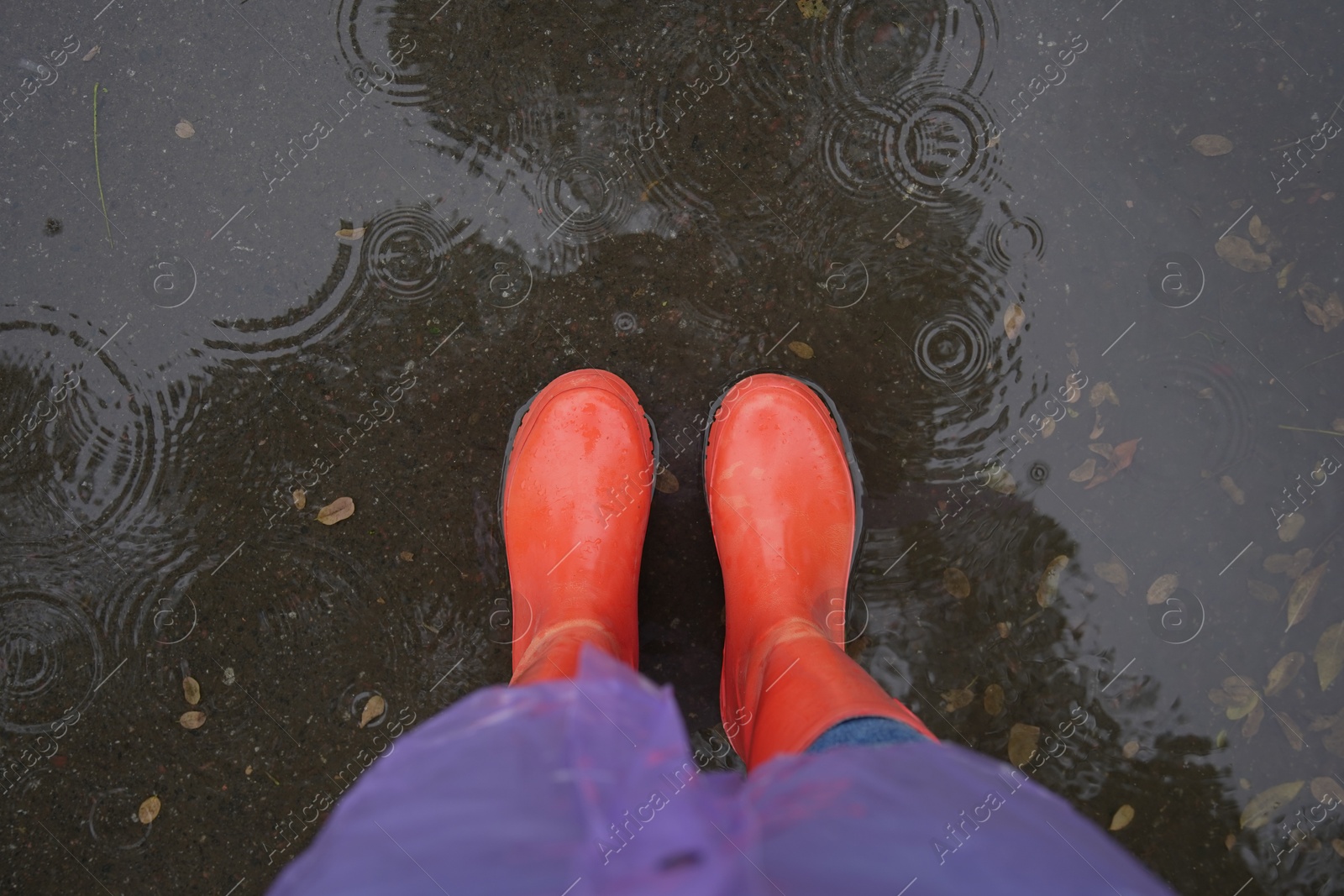 Photo of Woman wearing red rubber boots standing in rippled puddle, top view