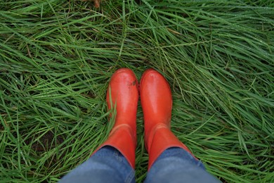 Photo of Woman in red rubber boots standing on green grass with dew, top view