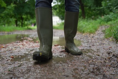 Photo of Woman in green rubber boots walking on muddy road, closeup