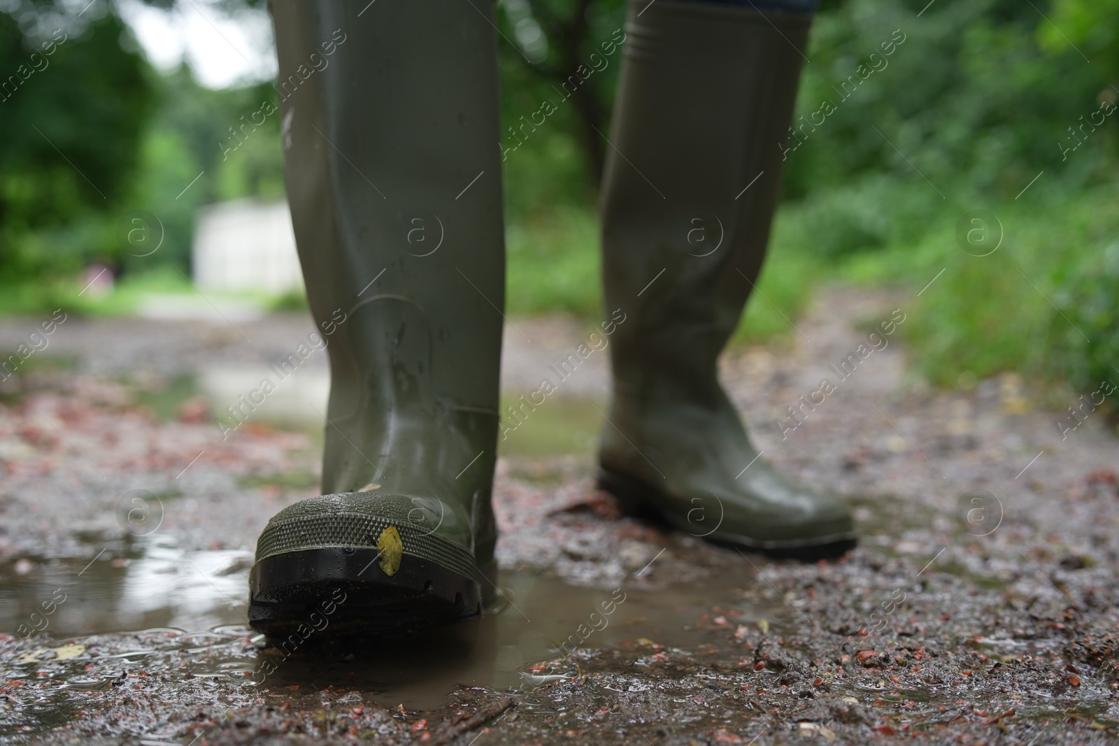 Photo of Woman in green rubber boots walking on muddy road, closeup