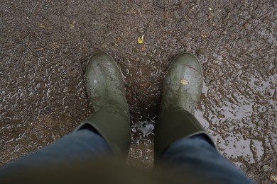 Photo of Woman wearing green rubber boots standing on muddy road, above view