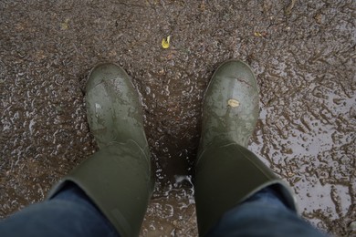 Woman wearing green rubber boots standing on muddy road, above view