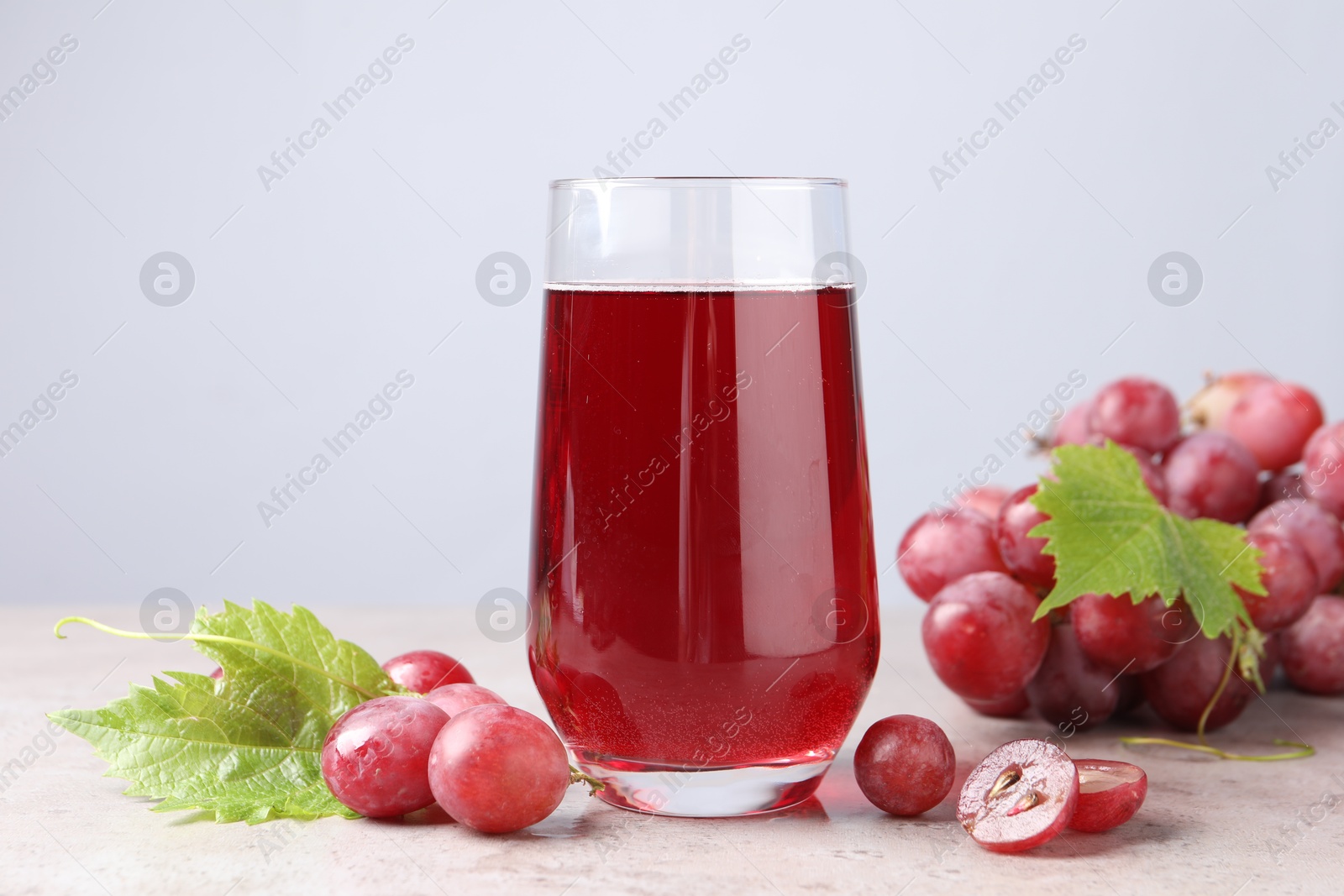 Photo of Ripe grapes and glass of tasty juice on grey table